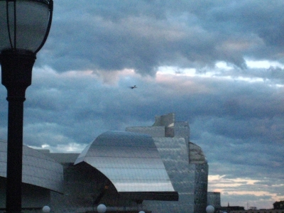 An airplane over the crumply silver art building. An airplane over the crumply silver art building.